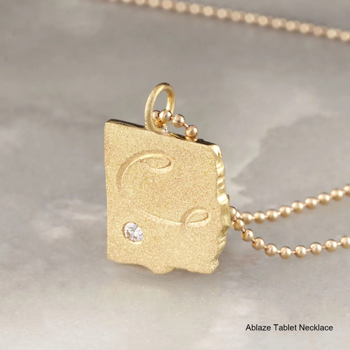 Gold necklace with a tablet-shaped pendant on a neutral background
