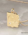Gold necklace with a tablet-shaped pendant on a neutral background