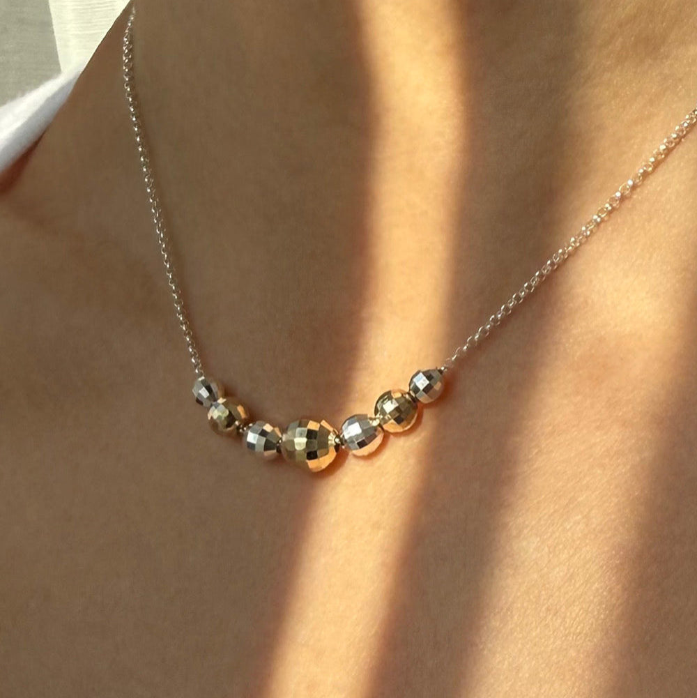 Necklace with gold and silver beads on a person wearing a white top.