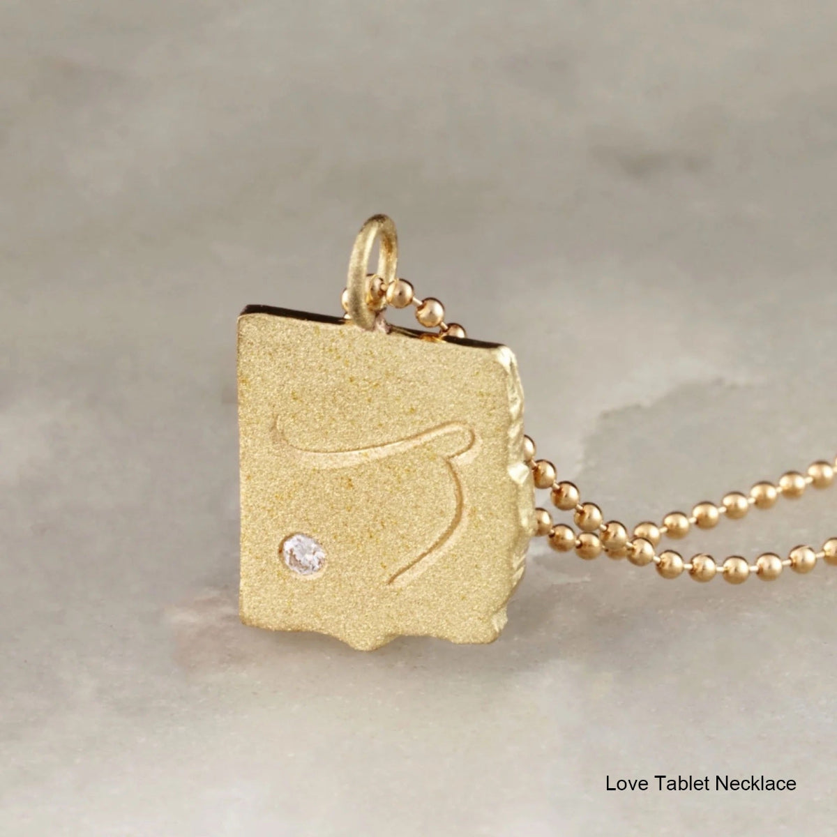 Gold pendant necklace with a diamond on a neutral background