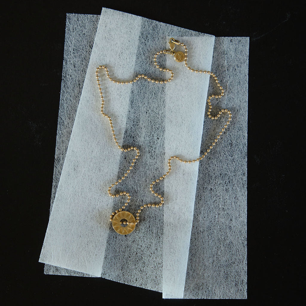 Gold ball chain necklace with round pendant displayed on translucent white paper